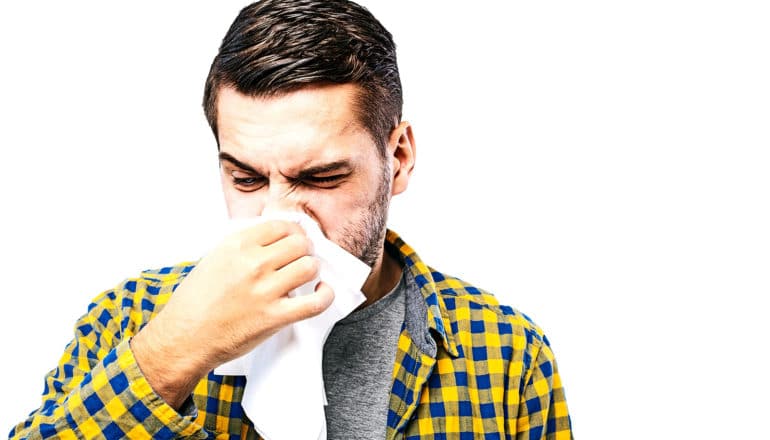 man in yellow and blue checked shirt blows nose against a white background