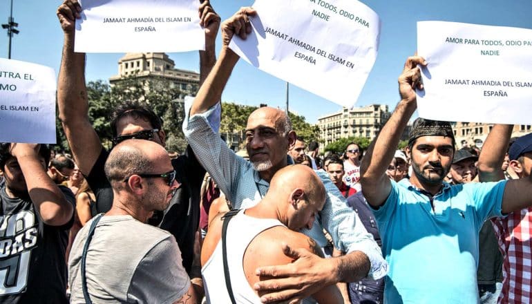 A man hugs Muslim protestors paying tribute to victims of terrorism, who are holding up signs that say "Love for all, hate for no one" in Spanish