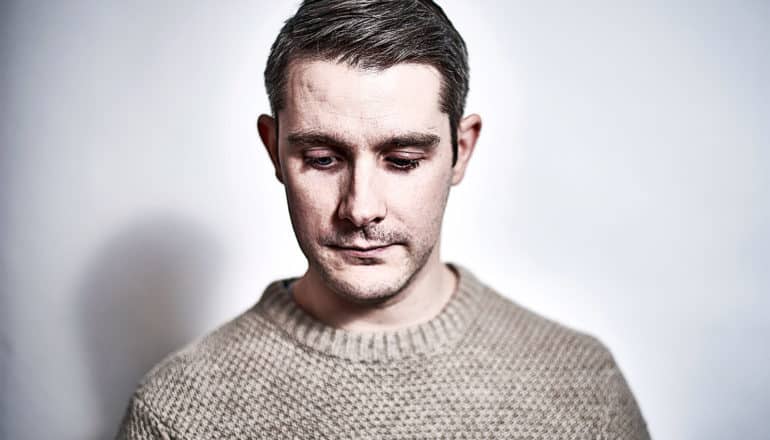 A man in a sweater looks down against a light gray background