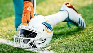 A football player kneels with his hand on his Miami Dolphins helmet