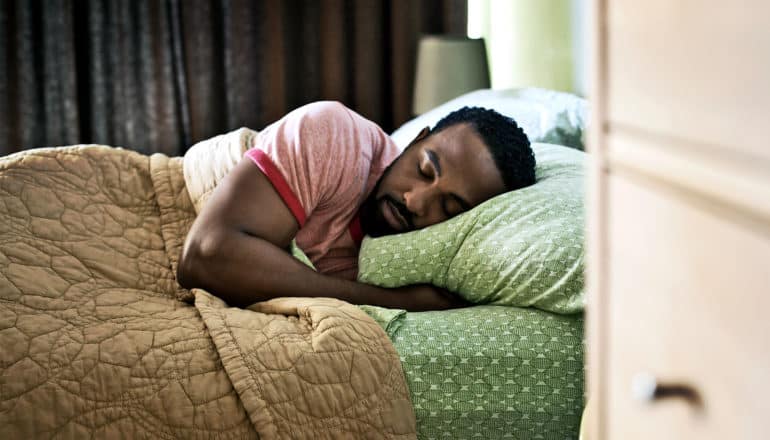 A man in a red t-shirt sleeps on green sheets