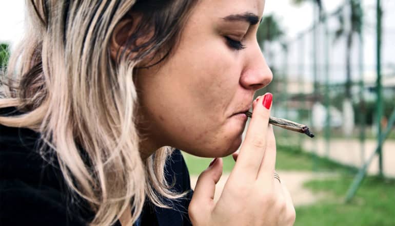 A young woman smokes marijuana outside
