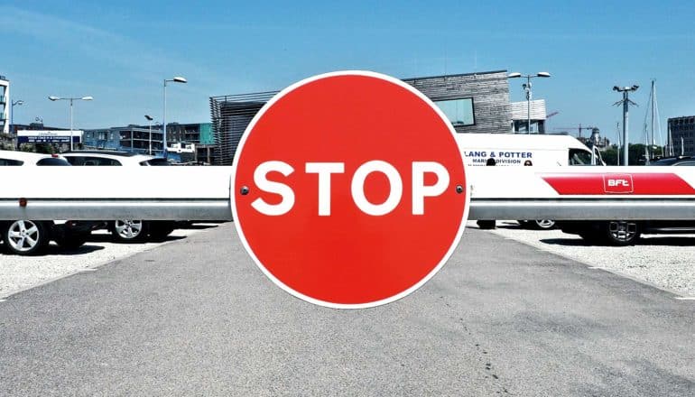 A stop sign on a barrier at the entrance of a parking lot, with a blue sky in the background