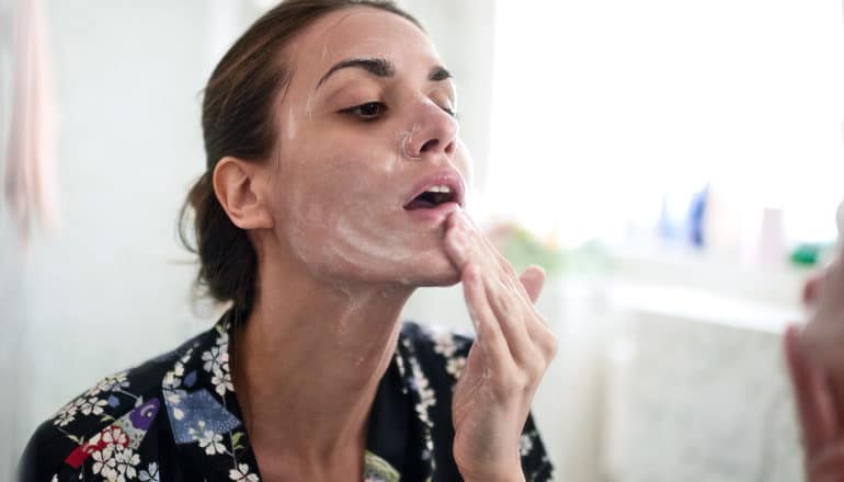 A woman rubs a skin cream onto her face