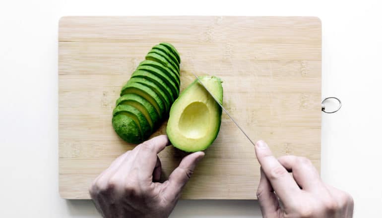 A person cuts an avocado on a wooden cutting board