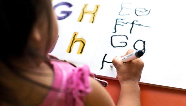 A preschool girl is writing letters in a workbook
