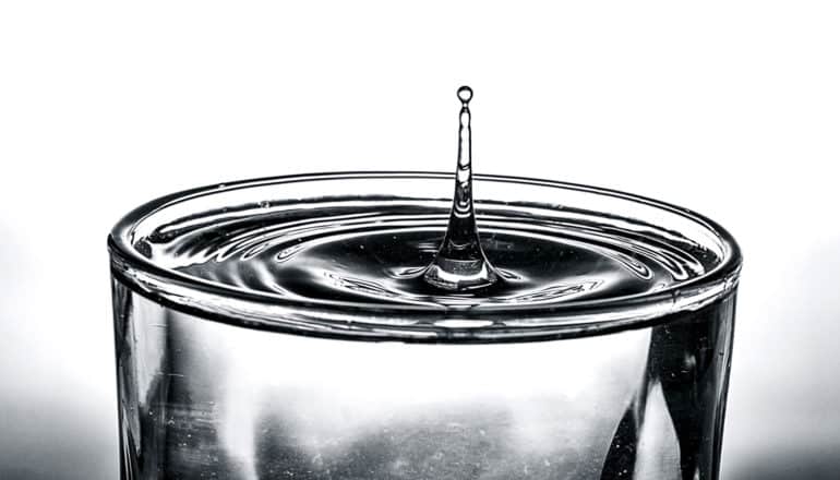 A glass of water with a droplet splashing upwards on a white background