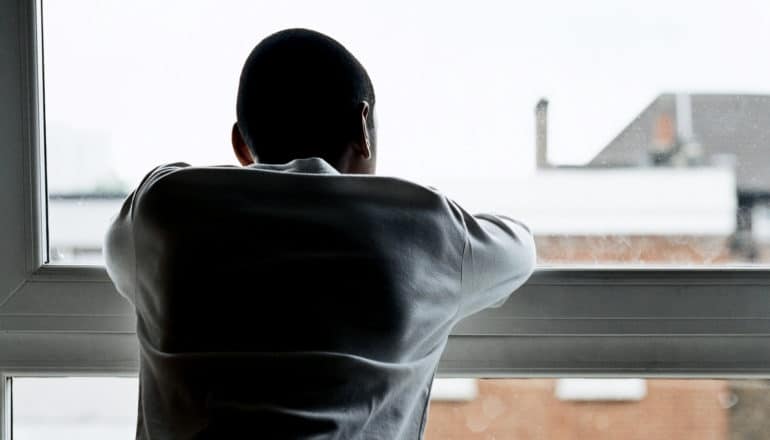 A teen boy looks out the window with his back covered in shadow