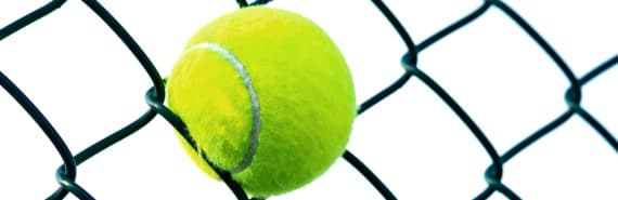 A tennis ball is stuck in a chain-link fence with white in the background