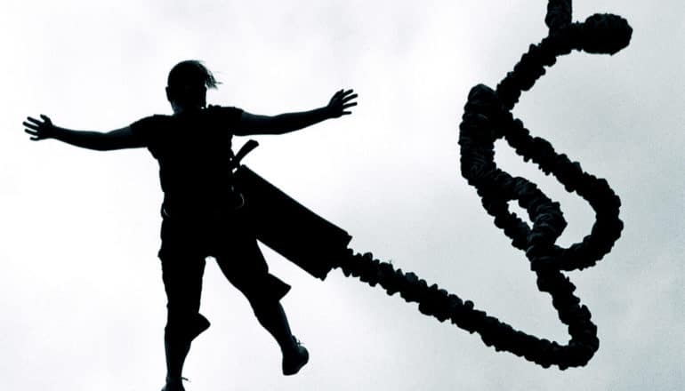 A person bungie jumps with their arms spread out in silhouette, with the cord twisting next to them in the air