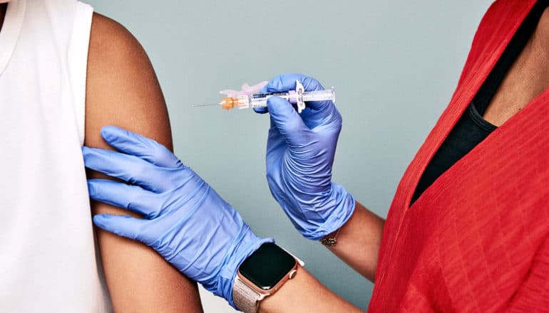 A doctor gives a patient a shot while wearing bright blue gloves