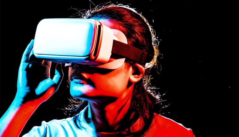 A person wears a virtual reality headset while covered in blue and red light against a black background