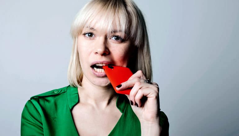 A woman in green bites down on her phone in frustration