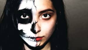 A young woman has half her face painted with black and white skull facepaint