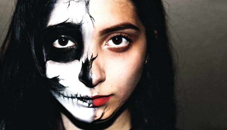 A young woman has half her face painted with black and white skull facepaint