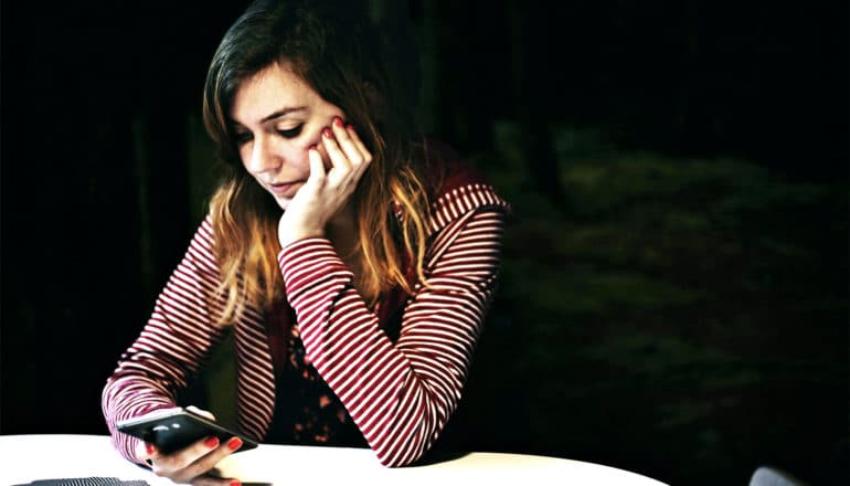 a young women in a striped shirt uses her phone by herself while resting her head on her hand