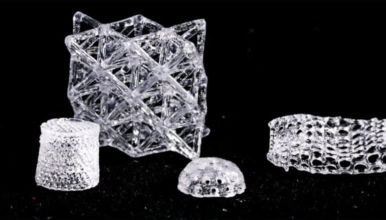 Several complex glass objects sit on a black surface, one a thimble-like object, another a dome with holes in it, another a cube-like lattice