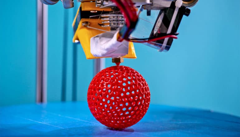 A 3D printer makes a red ball with many holes in it