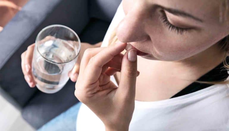 A pregnant woman takes a white pill while holding a glass of water