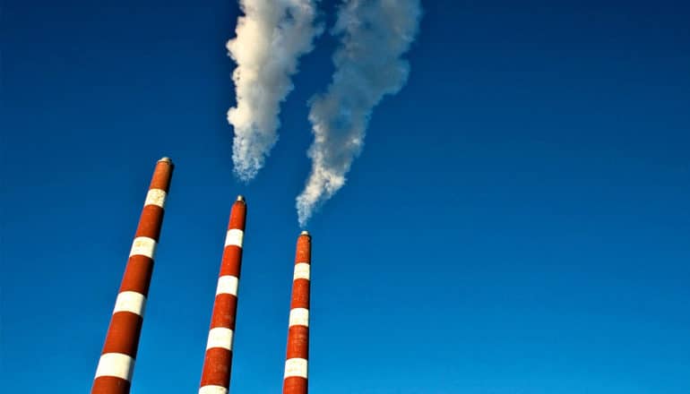 3 red and white striped smoke stacks from a power generation plant pump smoke out into a blue sky