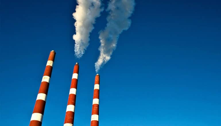 3 red and white striped smoke stacks from a power generation plant pump smoke out into a blue sky