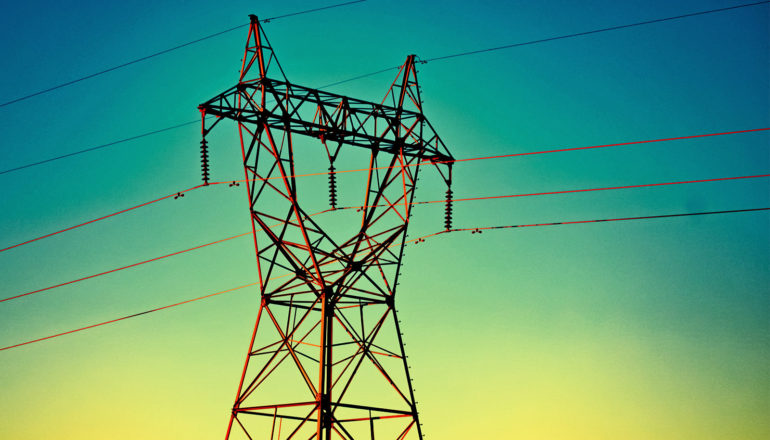 An electrical tower with wires coming out of it stands against a sunset-like background with blue at the top of the frame and yellow at the bottom