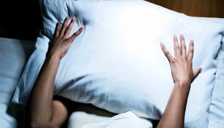 A woman holds her pillow over her face while trying to sleep
