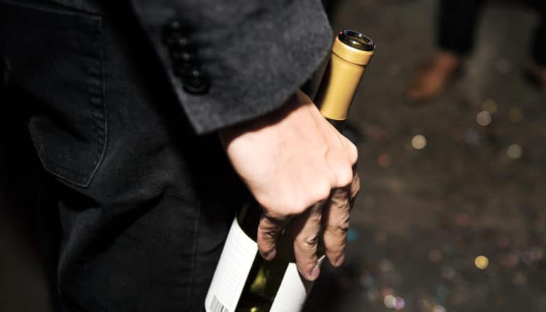hand of person outdoors at night holding open bottle of wine