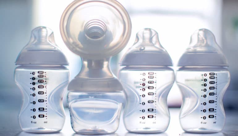 four baby bottles, one attached to breast pump flange