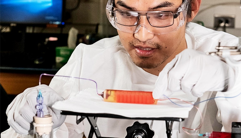 A researcher in white coat and gloves looks down at the small 3D-printed device, which could fit in his palm