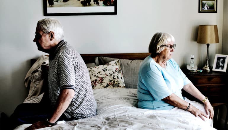 An older couple sits on a bed
