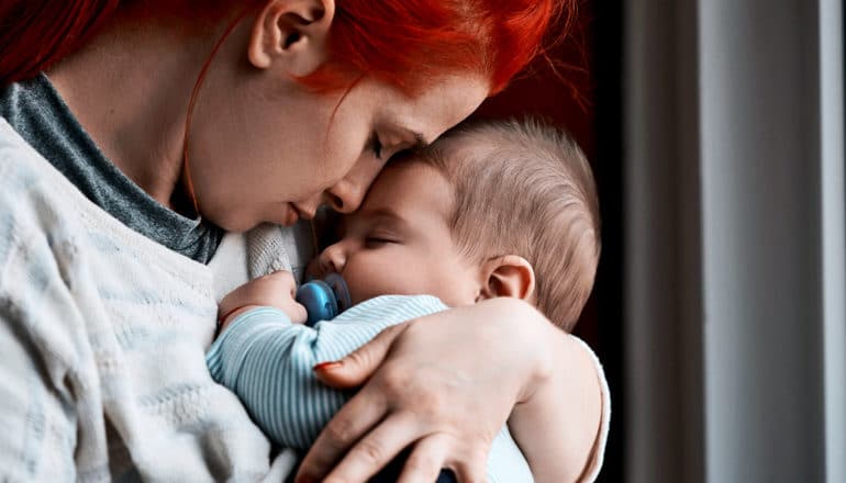 A mother with bright red hair holds her new baby close to her face