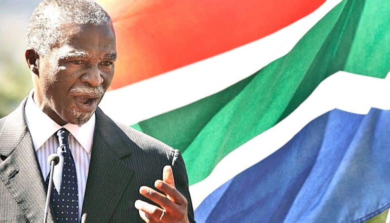 Former South African President Thabo Mbeki speaks while standing in front of a waving South African flag