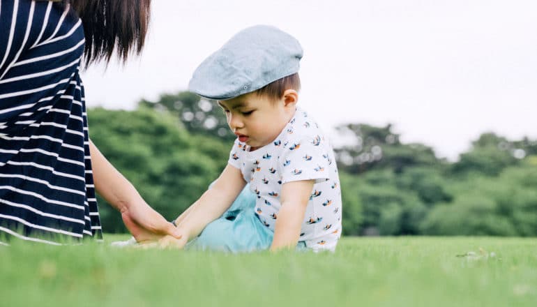 mom leans over and holds wrist of downcast toddler