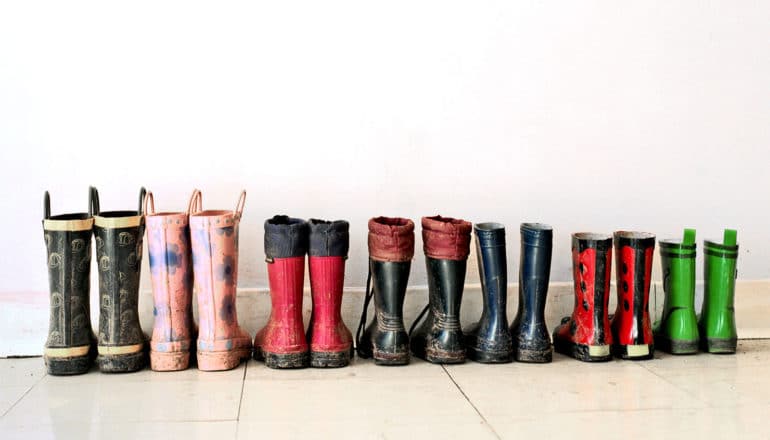 A row of smaller and smaller children's rain boots sit against a wall