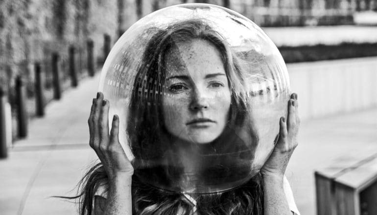 A woman holds a clear, bubble-like helmet over her head in black and white