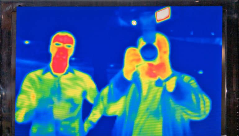 infrared tv shot of two people, one in mask, another holding camera