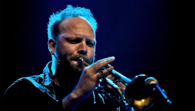 A jazz musician plays trumpet while standing in blue light