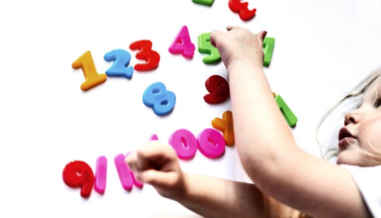 A child touches brightly colored plastic numbers on a white surface