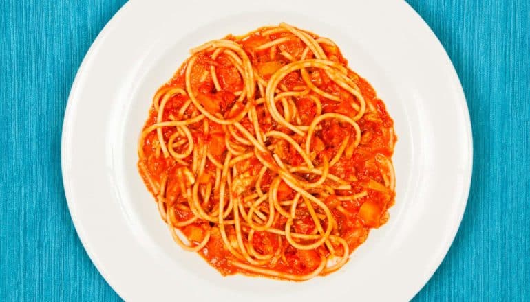 brightly lit spaghetti and tomato sauce in bowl on blue surface