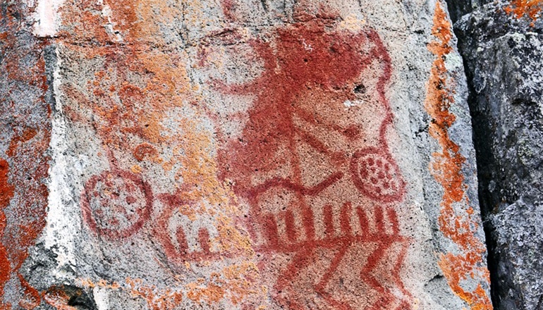 A rock wall is covered in red and orange paint, with different lines and shapes overlapping