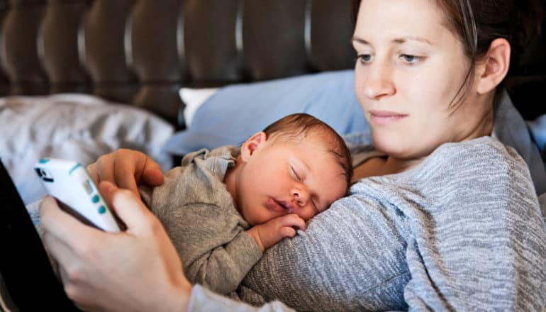 mother uses phone while baby sleep on her chest