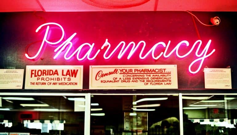 pink neon "pharmacy" sign over notices about generic drugs and store returns