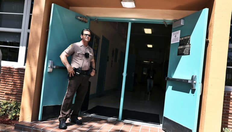 A security guard stands against a bright blue-green door at the entrance to a school