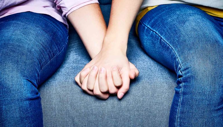 Two teens hold hands on a couch