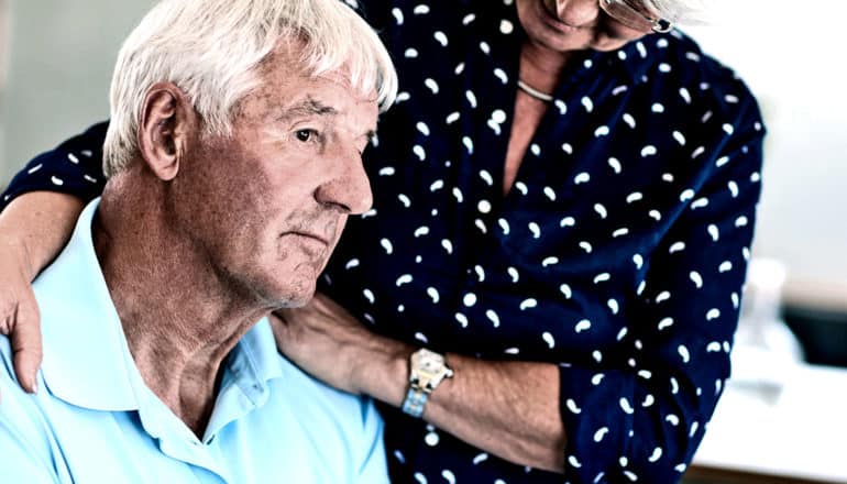 A man looks off into the distance as a woman in a dark navy shirt comforts him