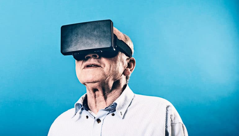 An older man wears a black virtual reality headset against a bright blue background