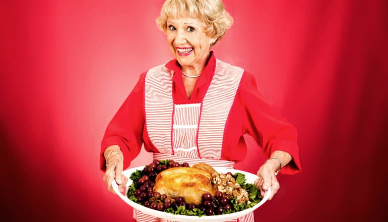 smiling person in 1960s festive apron holds turkey on platter