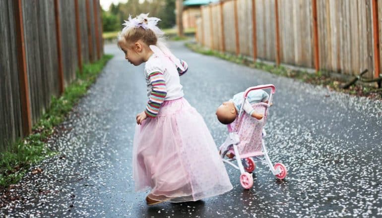 child in pink dress in driveway with doll and toy stroller