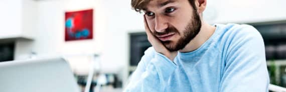A man in a blue shirt looks at a computer with skepticism or even disgust